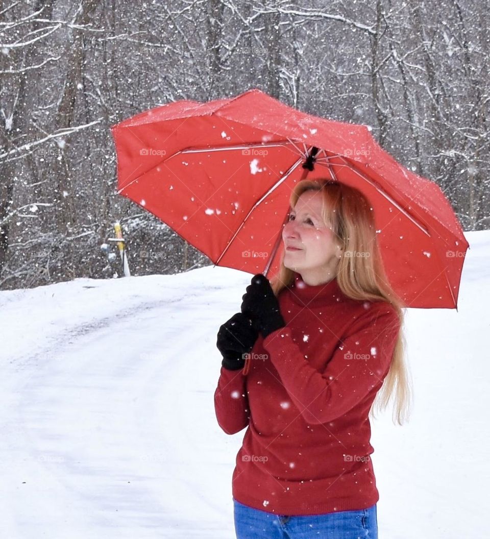 Woman in a red sweater with a red umbrella in the snow