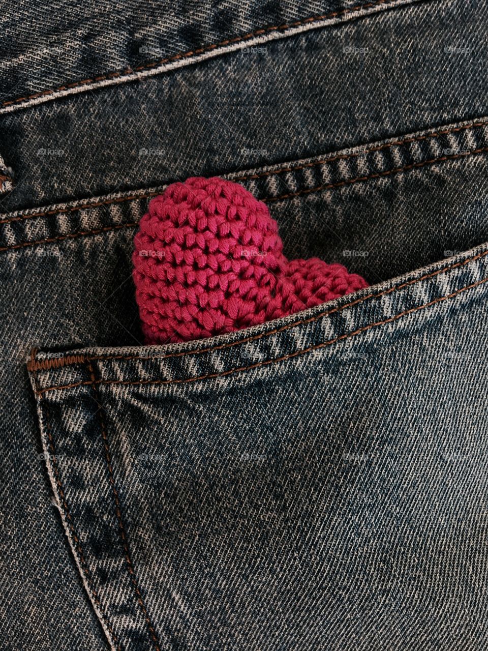 small red knitted heart in the pocket of blue jeans, a top view