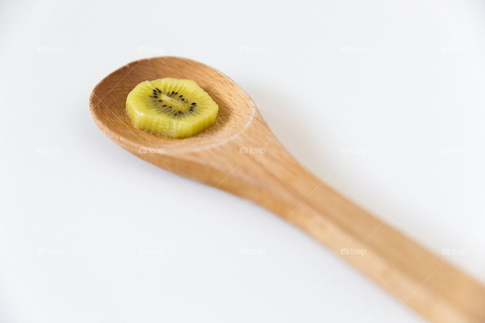 Minimalist image of sliced fresh kiwi fruit on a wooden spoon with a white background.