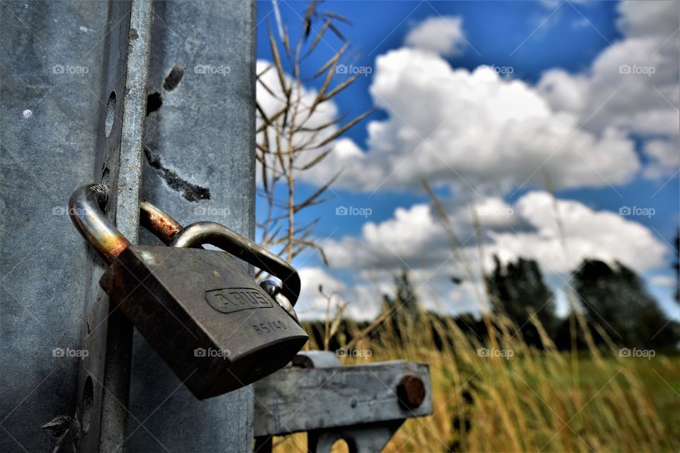 Lockdown in nature padlock on steel fence in field with clouds