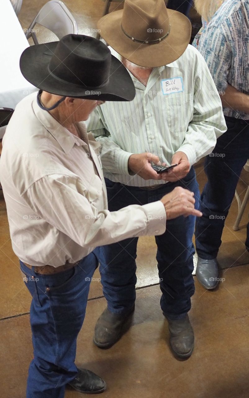A pair of old cowboys doing some texting together. 