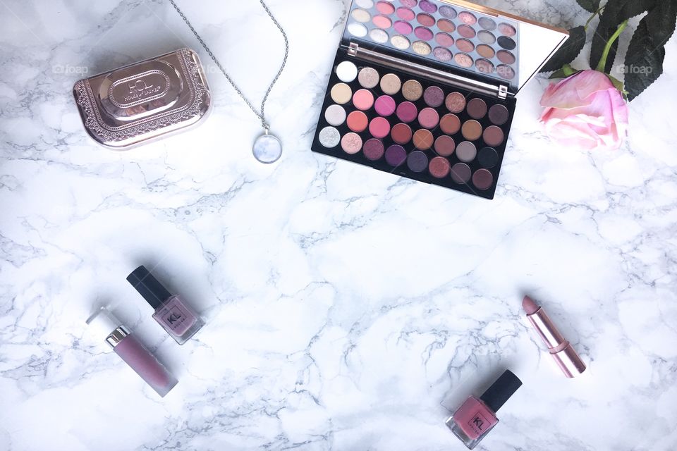 Makeup flat lay on a marble background, light pink, eyeshadow palette, nail polish and lipstick.