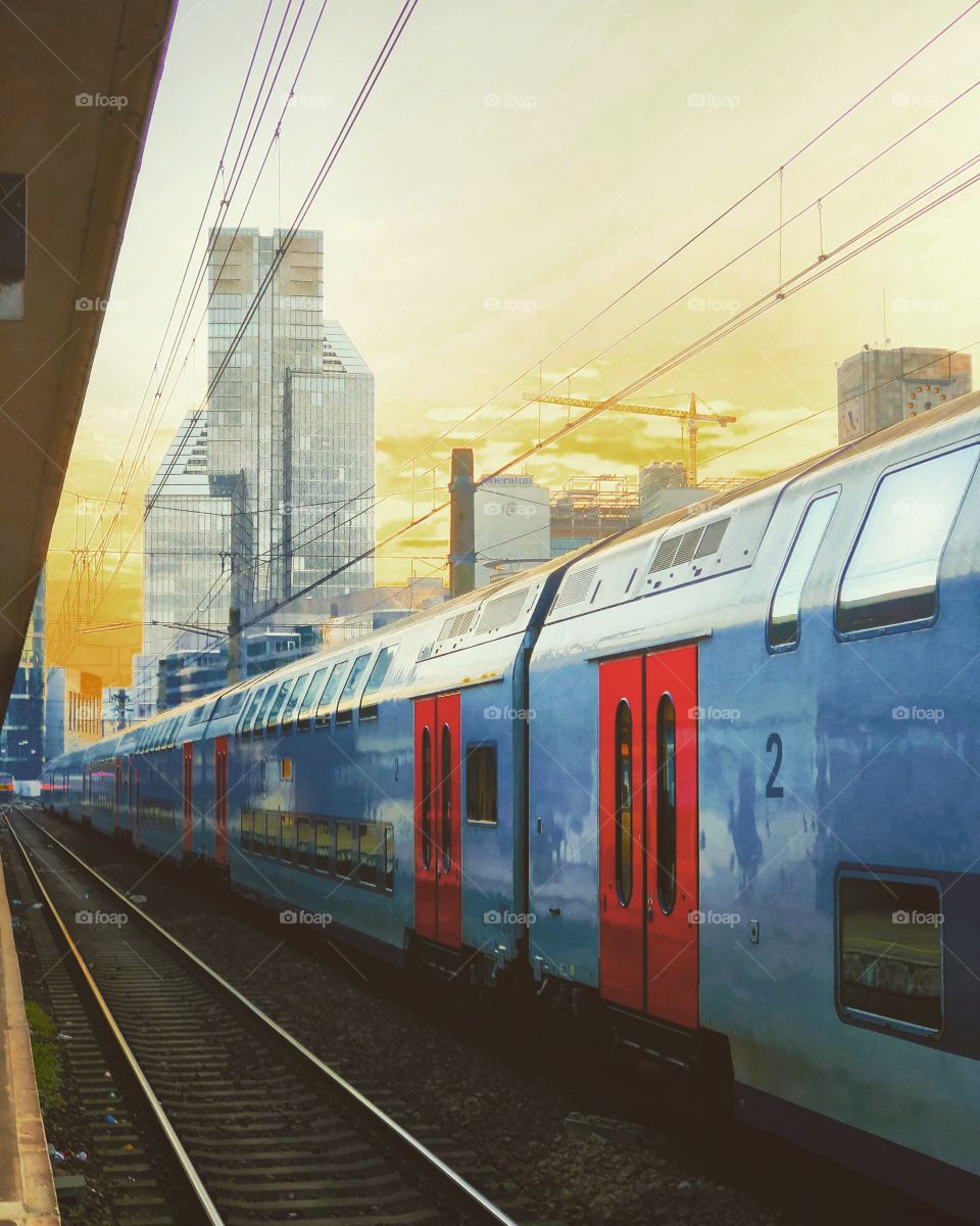 Train in the railway station of a modern city under a surreal Golden sky with the skyscraper office towers of the business district in the distance