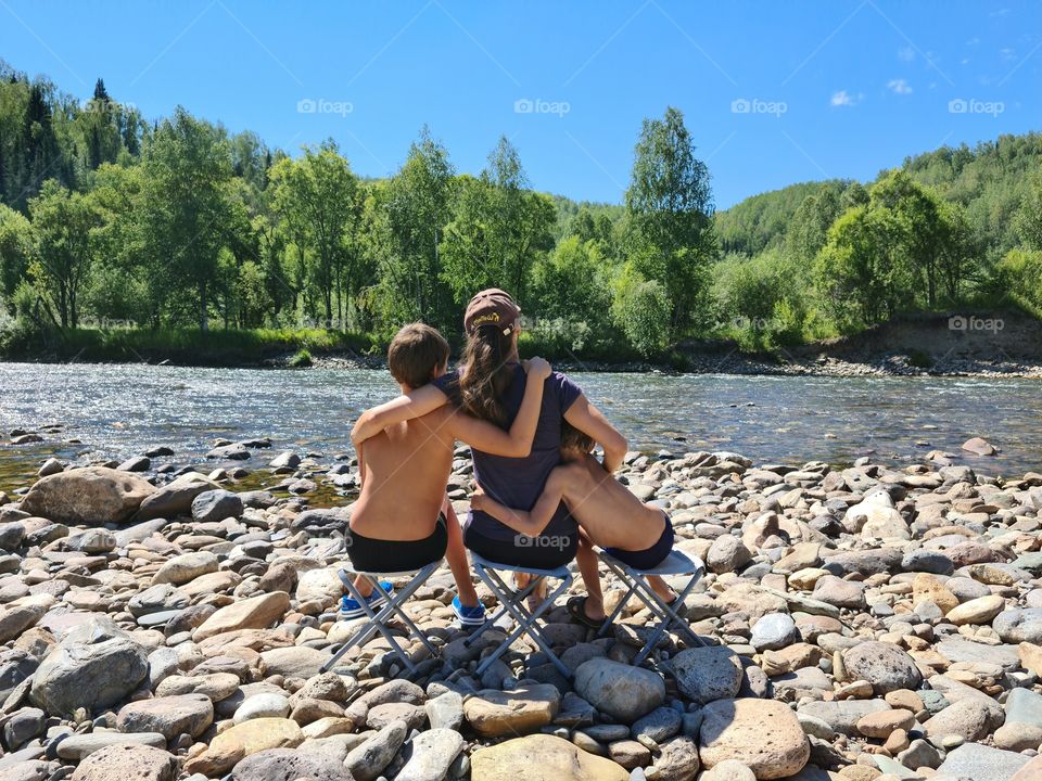 woman with children sit on the river bank on tourist chairs