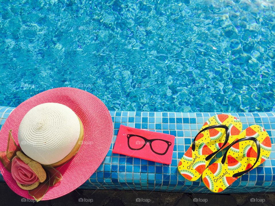 Flip flops with watermelons,pink sunglasses case and pink summer hat near the pool