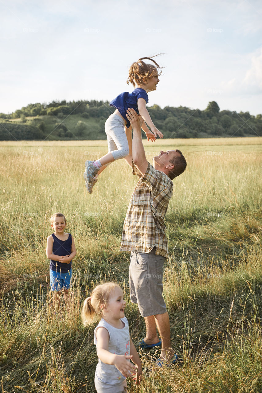 Father tossing little girl in the air. Family spending time together on a meadow, close to nature. Parents and children playing together. Candid people, real moments, authentic situations