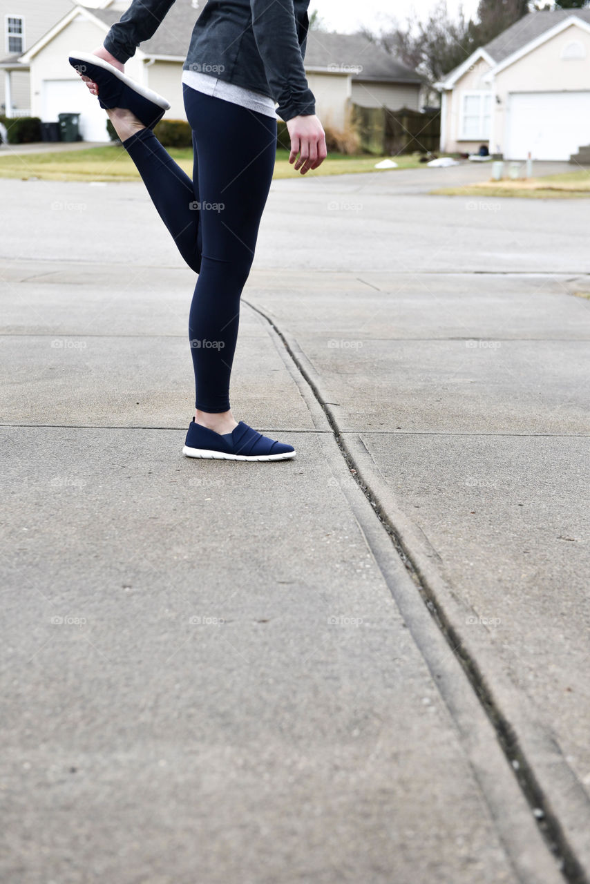 Bottom half of a woman standing and stretching on a residential street before a run