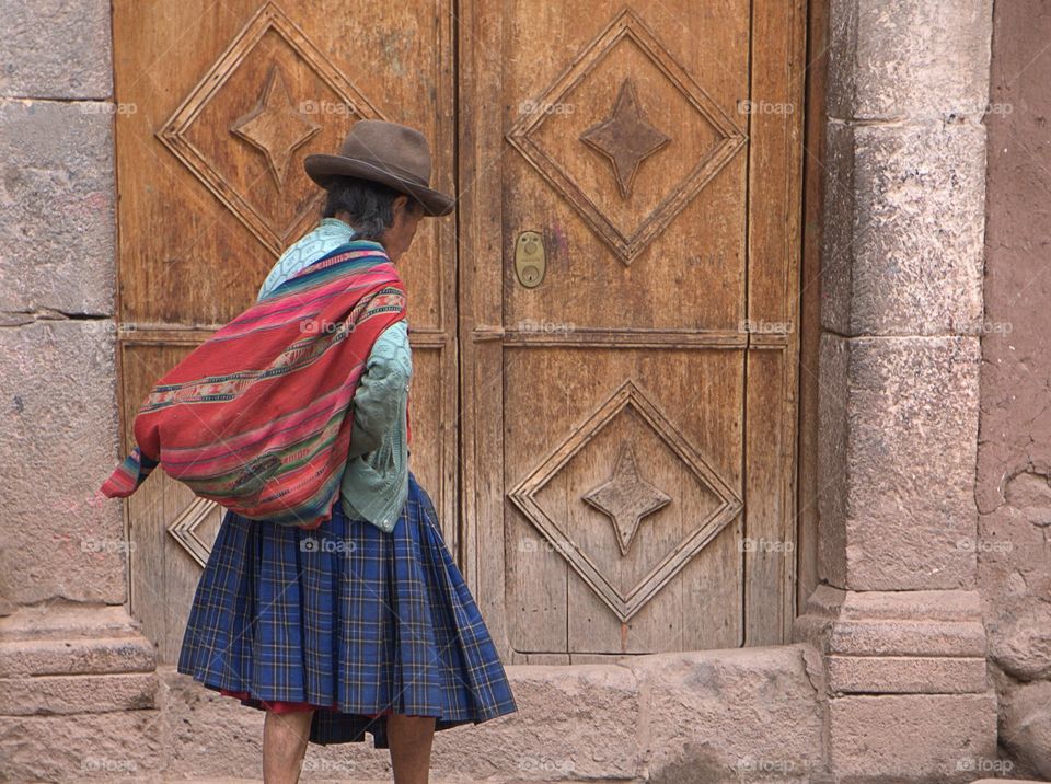 A back view of an Inca woman in colorful traditional dress walking down the street in Pisca, Cusco, Peru.