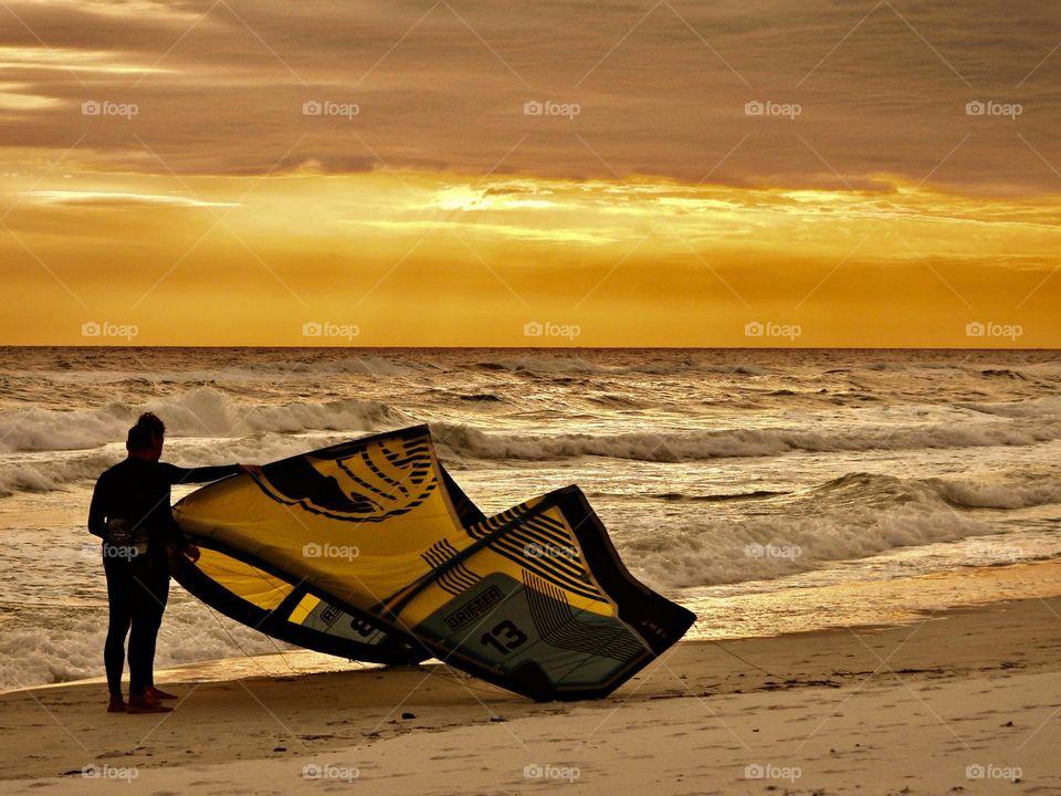 Windsurfer prepares his wind sail to resurface the bay waves during a magnificent, golden colored sunset