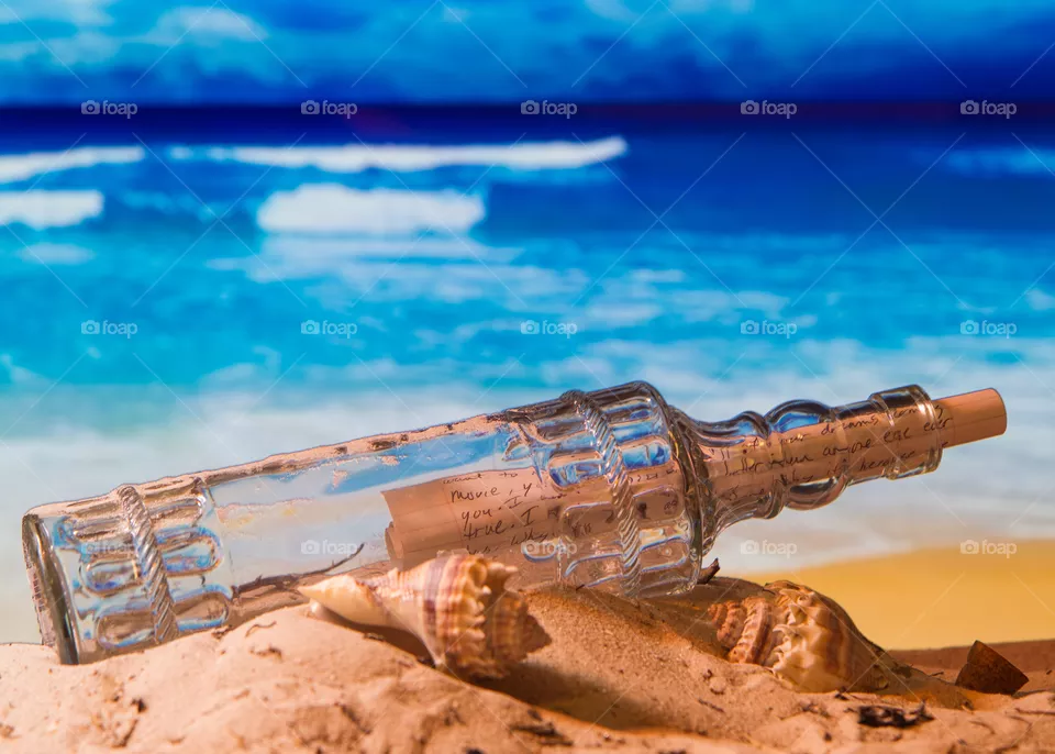 glass bottle used to send love letter on a sandy beach at sunset with blue water and waves crashing in the background
