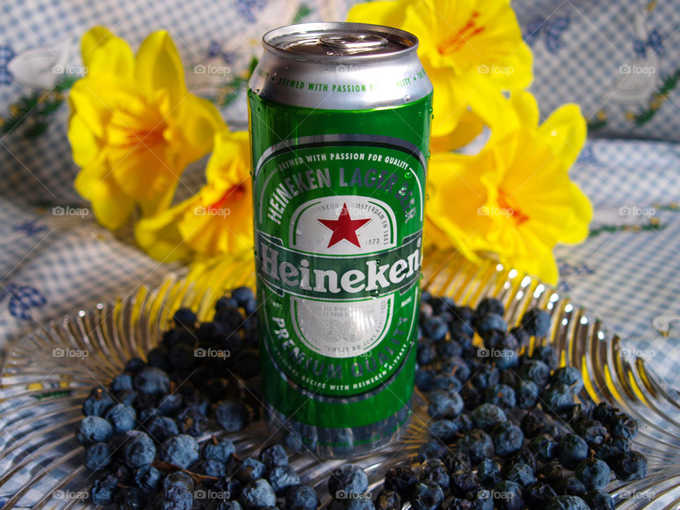 Heineken in glass dish and checkered tablecloth with yellow flowers, blue sloe, water drops.