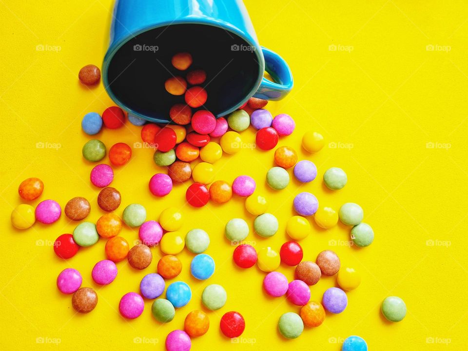 colored and round candies spill out of the blue cup