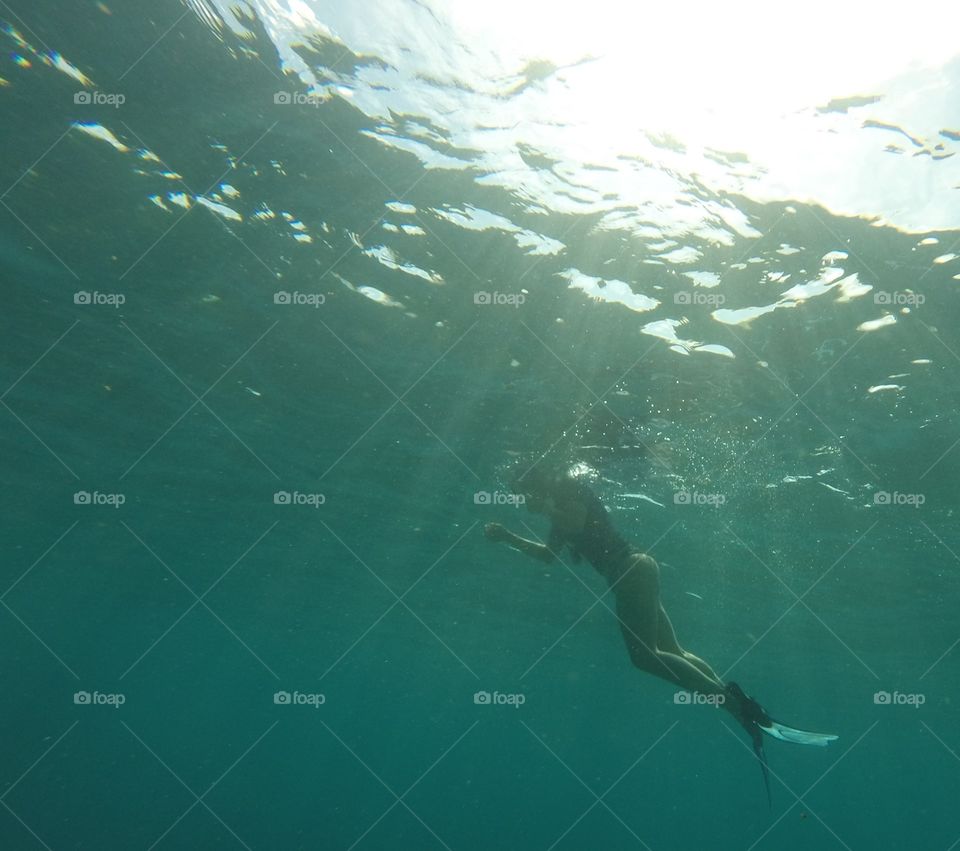 Snorkeler seen from underwater with sun rays coming from water surface.