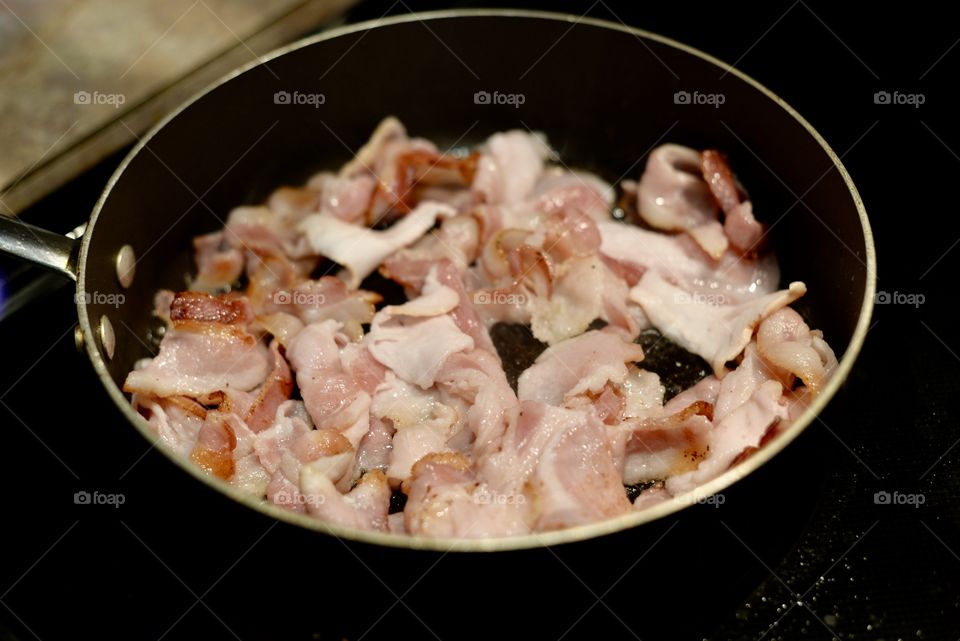 Close up of fresh bacon in a frying pan 