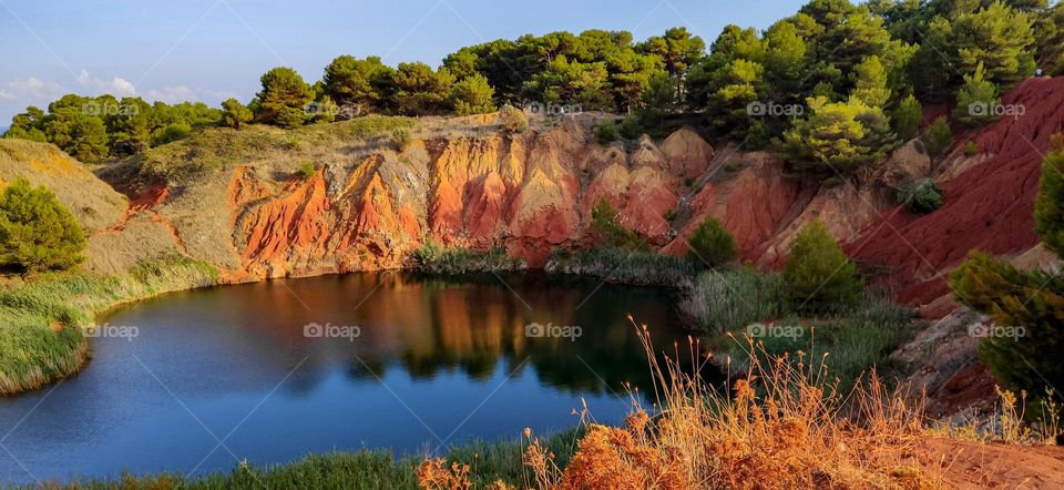 Beautiful view of a colorful clay quarry with water and trees in Italy, close-up side view.