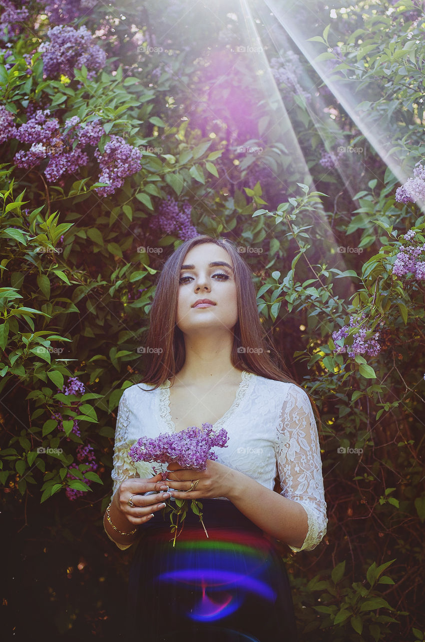 Portrait of young beautiful woman with bouquet of lilacs in pre sunset light in spring garden.