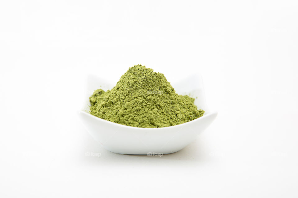 Health product - barley grass green powder in white bowl on white background macro closeup