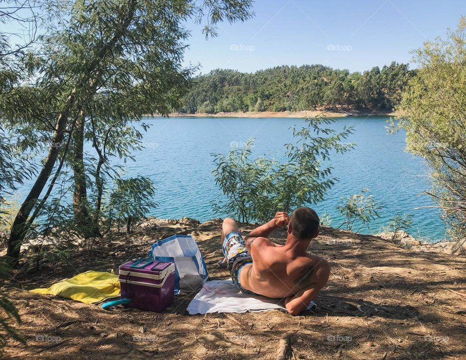 A man relaxes in a shady spot by the river on a clear summer’s day