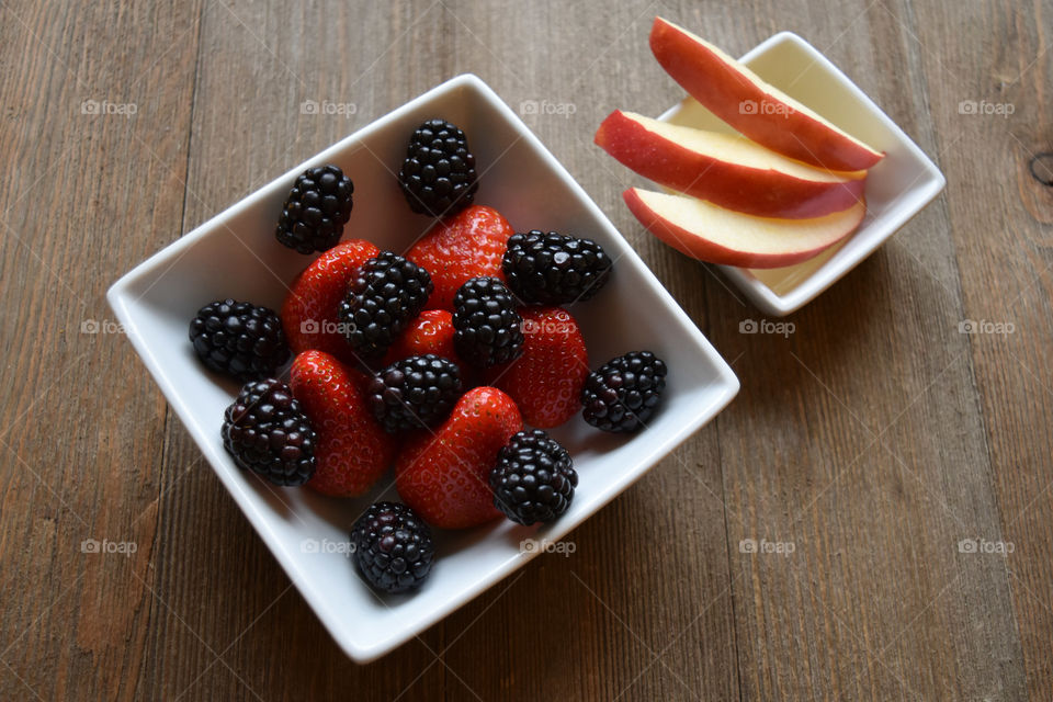 Bowl of strawberries and blackberries with apple slices on a wood background