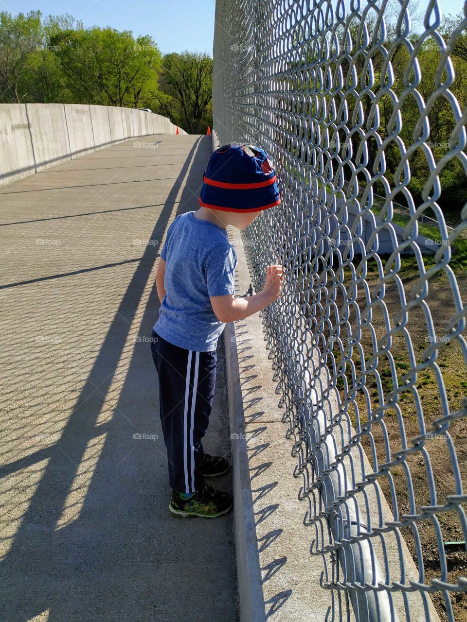 Curious boy looking through a fence on a long walking bridge