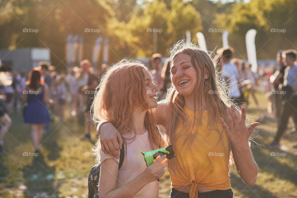 Portrait of happy smiling young girls with colorful paints on faces and clothes. Two friends spending time on holi color festival. Real people, authentic situations