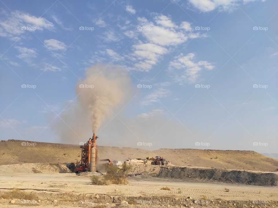 smoke rising in the cloudless sky and a desert a small asphalt factory