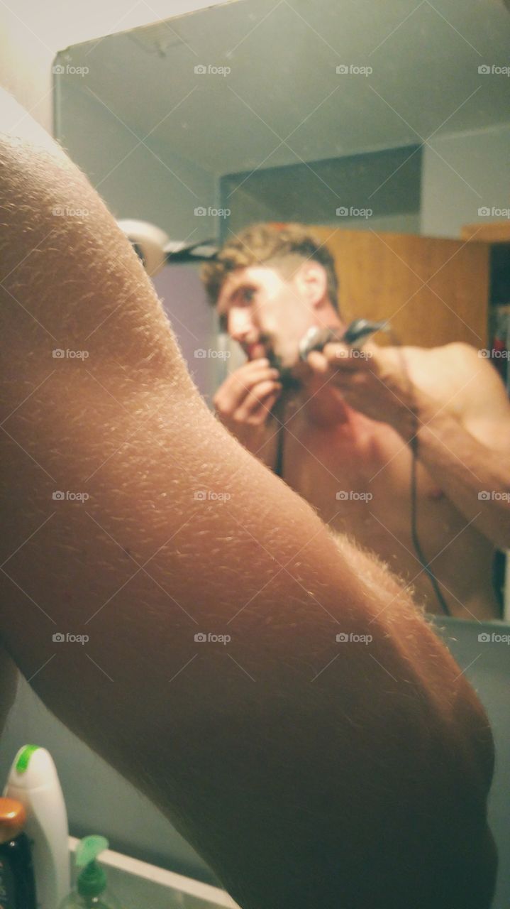Young man shaving with trimmer in front of mirror bathroom
