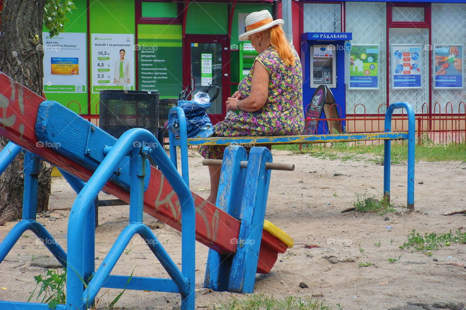 an elderly woman is sitting on a bench near a playground