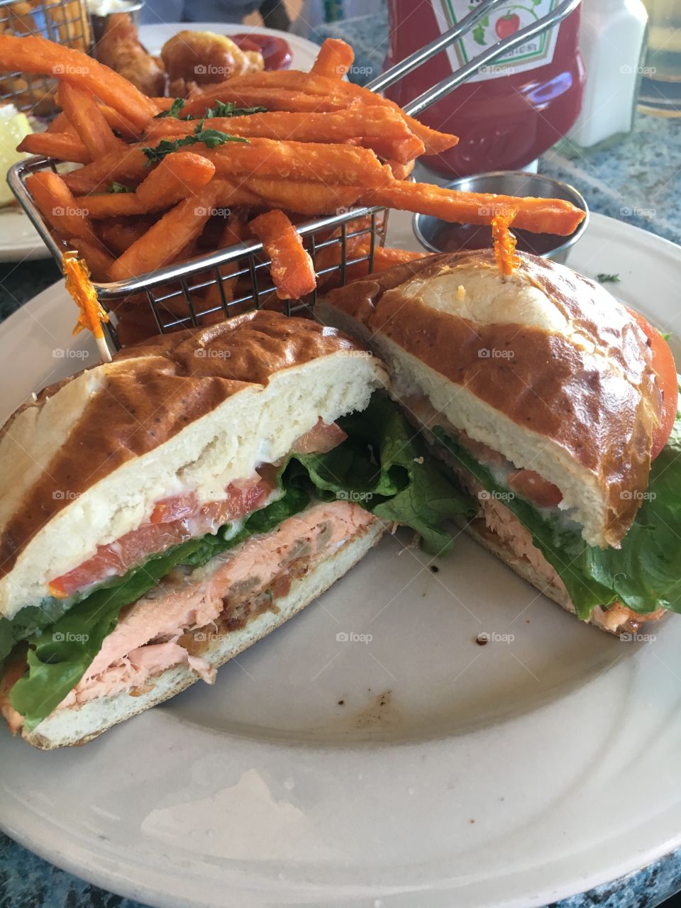 Cross-section of a delicious gourmet salmon sandwich with a basket of fresh sweet potato fries on the side!