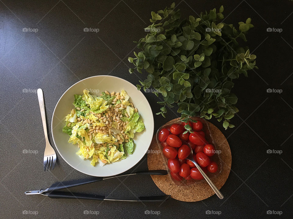 Food flatlay at the black table. Plate with fresh salad and box with tomatoes cherry