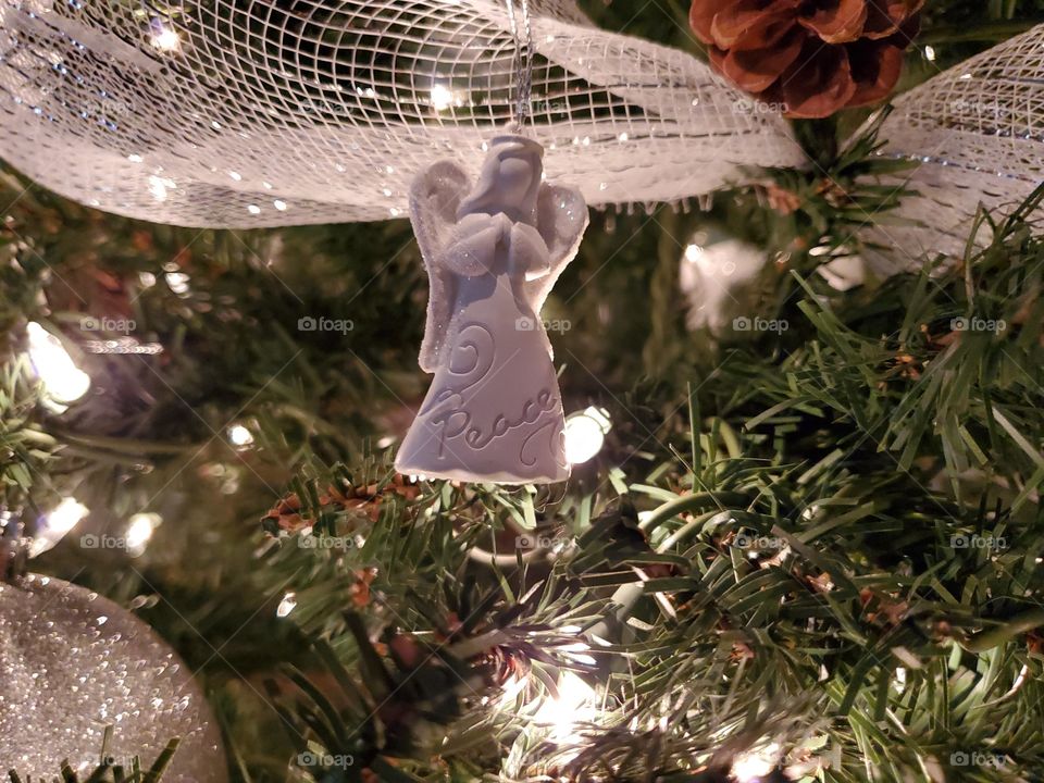 White Angel of peace Christmas ornament hanging on Christmas tree with white Christmas lights