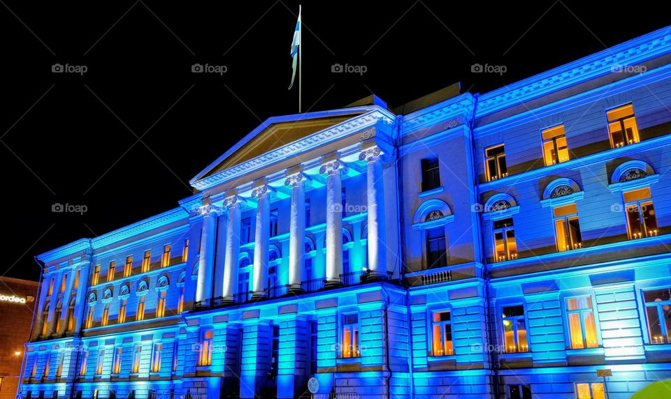 Old renovated white palace building with columns at the facade lighted with mystical blue neon light in late night darkness