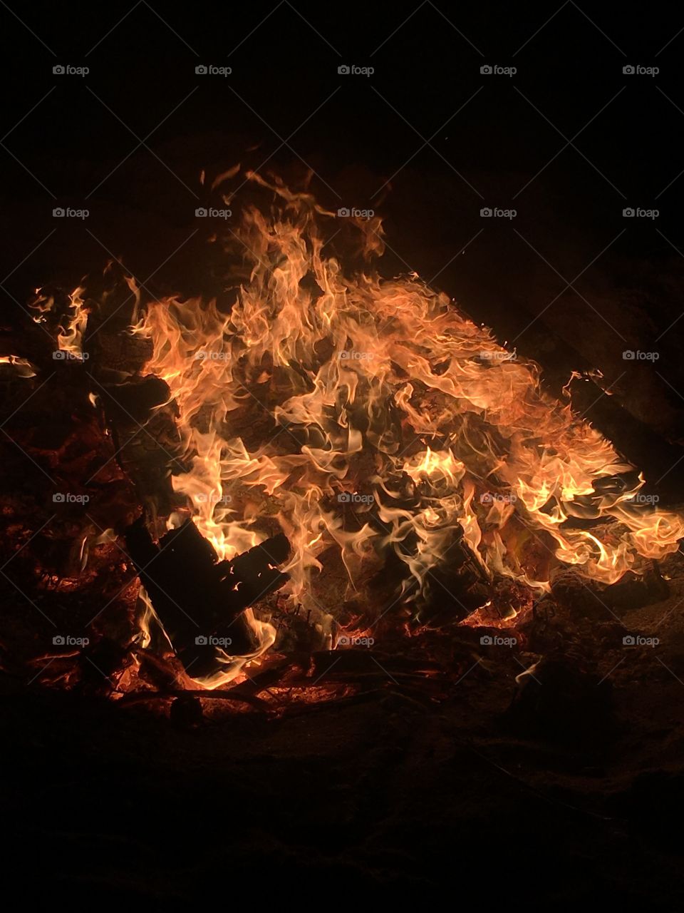 A large beach bonfire simmering through the mountain of wood. 