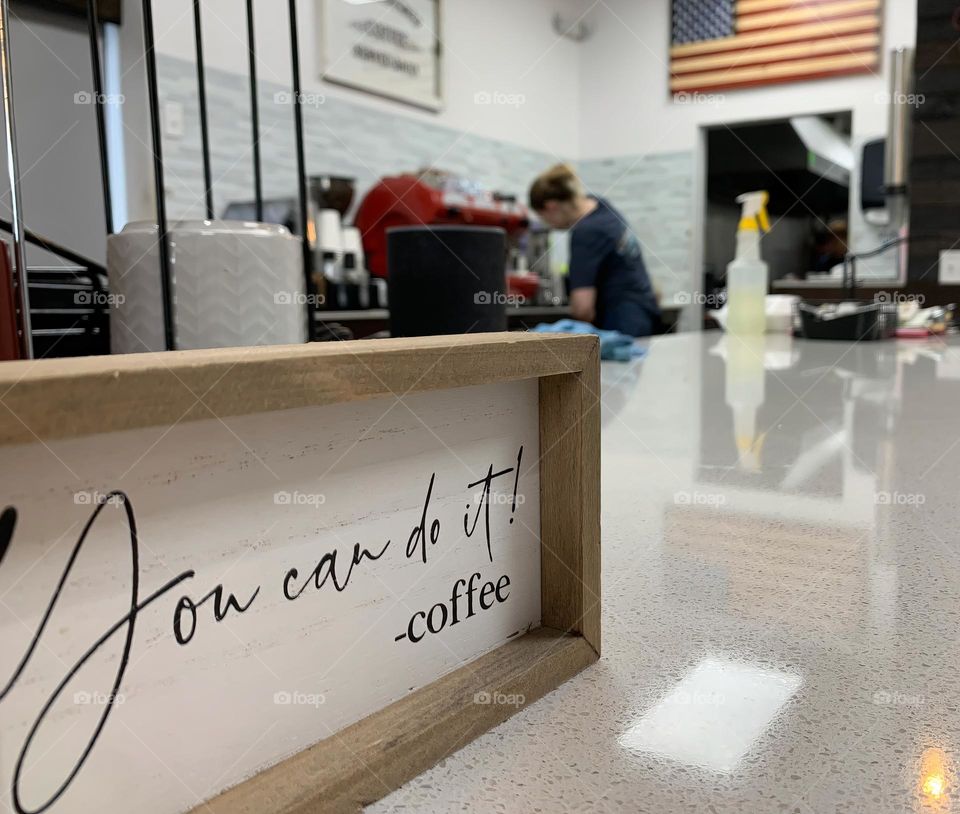 « You can do it! -coffee » sign in the foreground focus at a coffee shop interior small business unique brand with coffee maker workers on the move with happiness seeing the coffee cups holder.