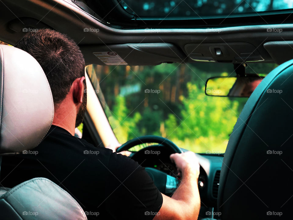 Young man driving a car through the forest during the road trip 