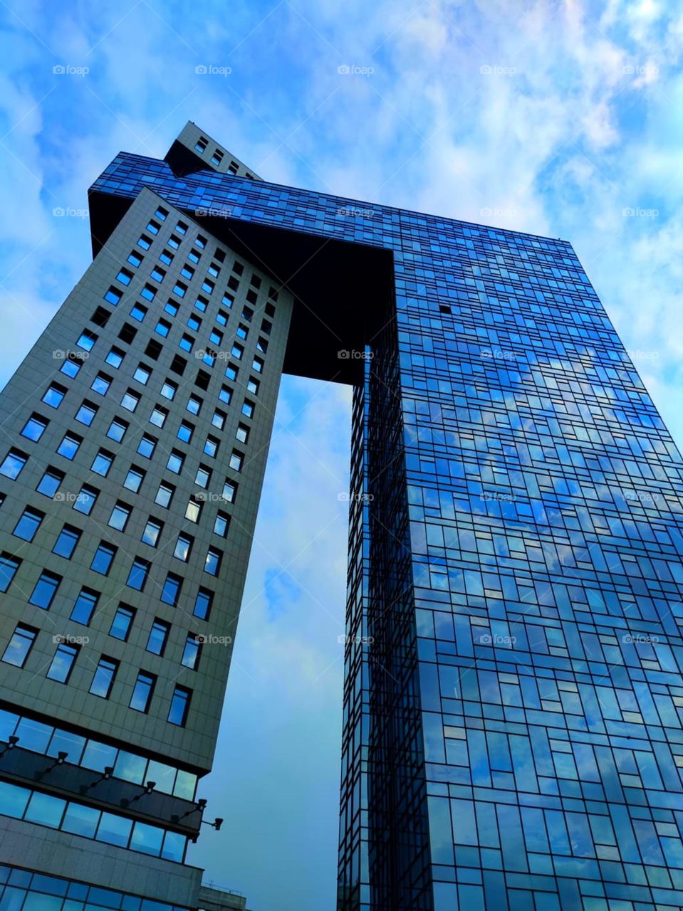 Modern architecture. A skyscraper of two buildings against a blue sky with white clouds. White clouds are reflected from the windows of a skyscraper