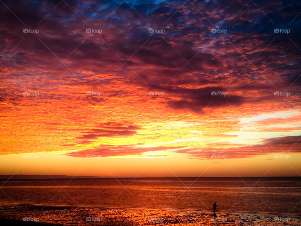 Person on beach at beautiful orange sunrise with approaching storm and clouds