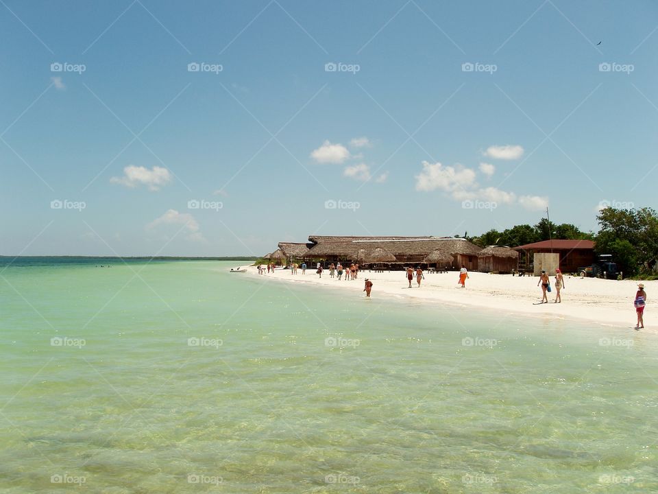 a transparent sea and people walking in the white sand of the beach