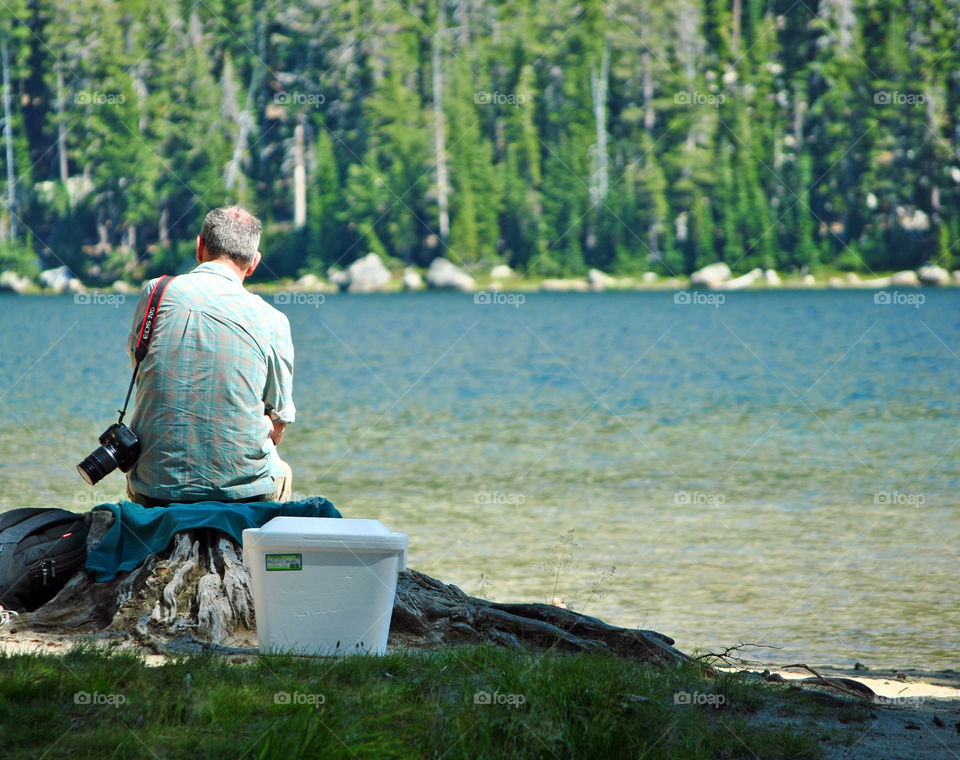 Old man carrying a camera on his shoulder sitting by the lake relaxing