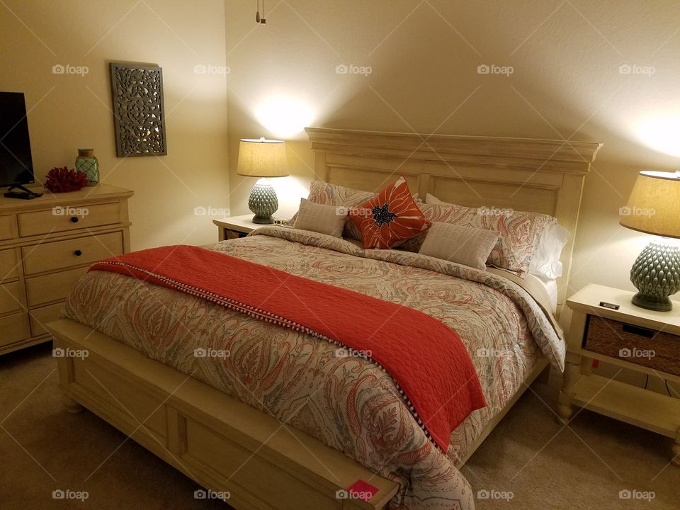 master bedroom with soft lighting, light furniture, orange and cobalt blue accents