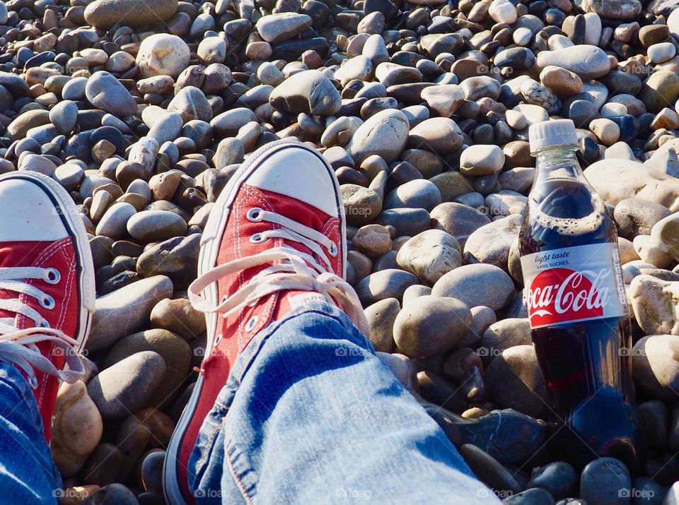 A bottle of Diet Coke on the beach with red sneakers.