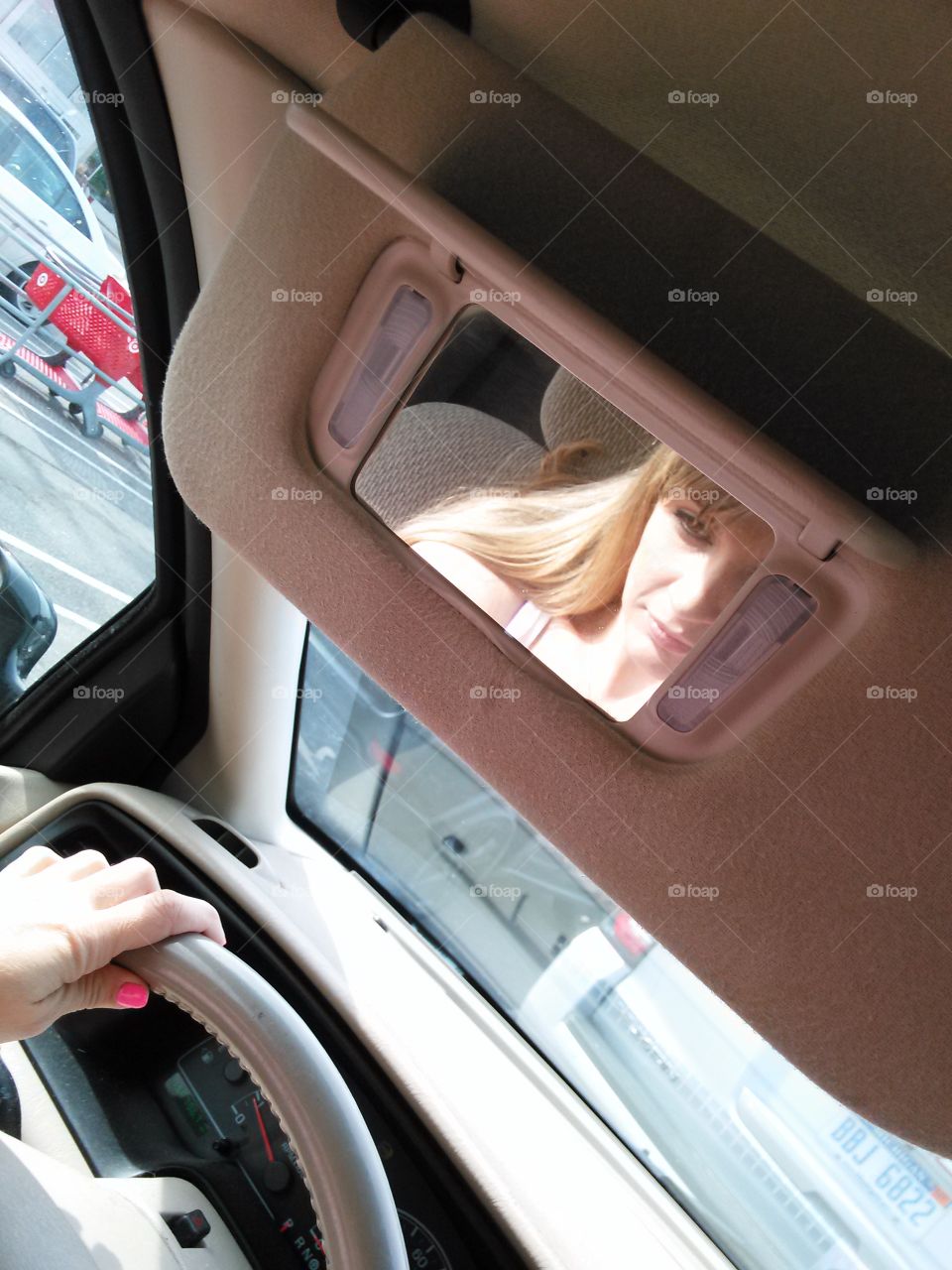 Self Reflection. Woman's reflection in a car visor mirror and hands on a steering wheel. 