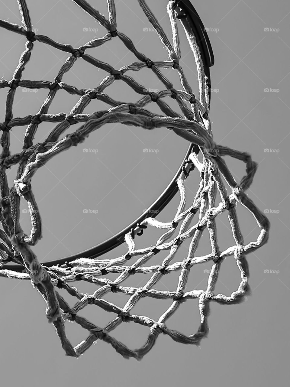 Looking up at a basketball hoop net in black and white on a clear day at the park, abstract and graphic 