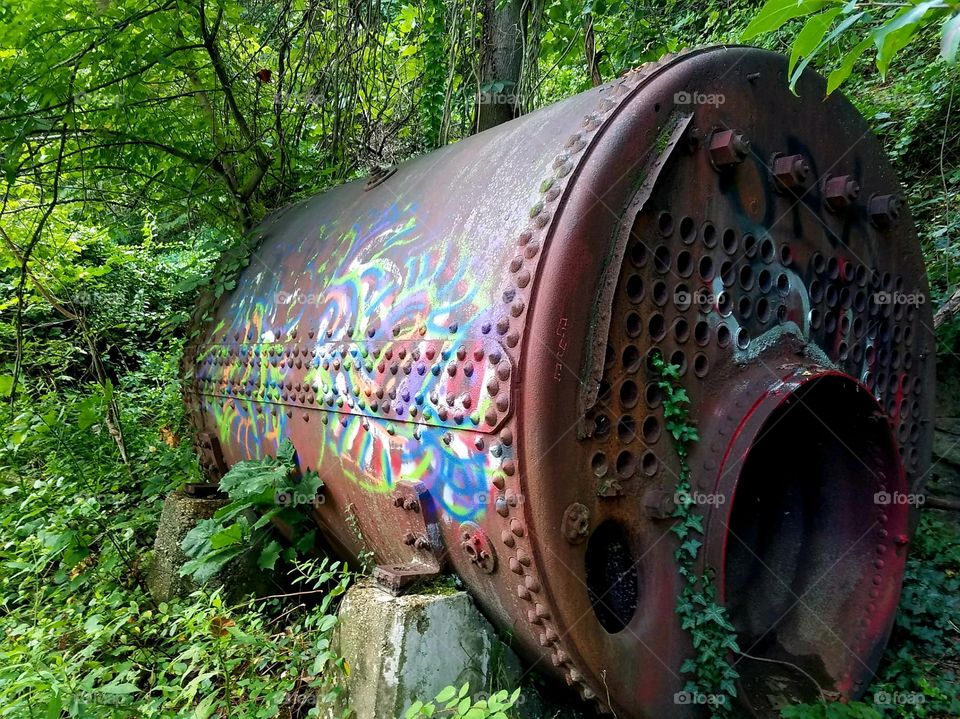 Old rusty drain pipe left abandoned in woods with colorful tagging.