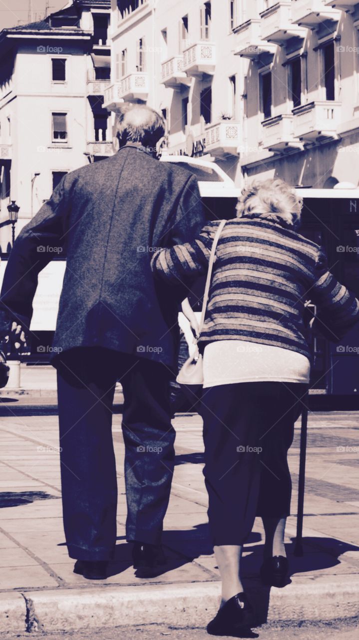 Old couple helping each other to cross the road