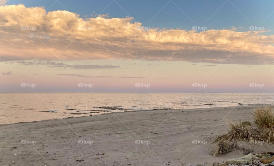 Liquid Fresh water Lake Eerie on Cedar Point shoreline.  sandy, rocky beach with purple, pink and blue sunset sky divided by a white puffy cloud 