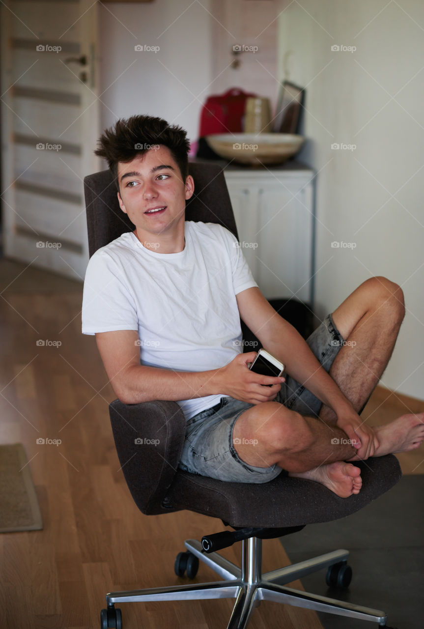 Relaxed boy holding smartphone sitting in chair at home