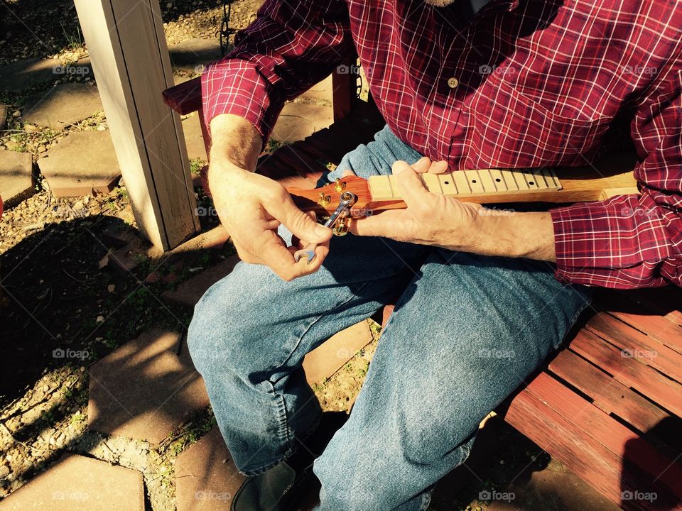 A man, my husband, putting the tuning machine on the  cigar box guitar that he is making. 