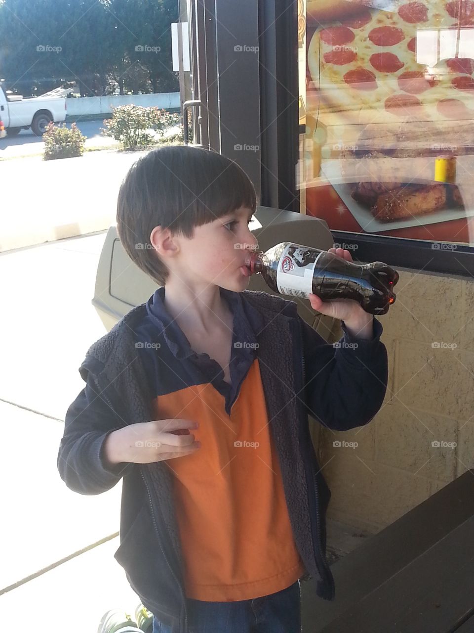 Young boy drinking a soda outside a building.