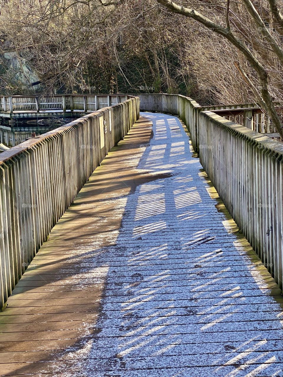 Snow and shadows on a boardwalk around a quarry lake at a local park 